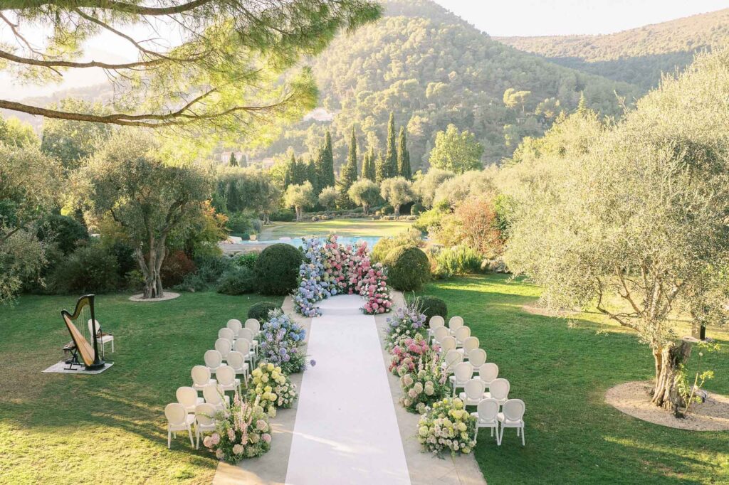 Outdoor wedding ceremony setup at a French Riviera spa resort Château Saint-Martin and Spa with white aisle chairs, floral arrangements, and mountain views at sunset.
