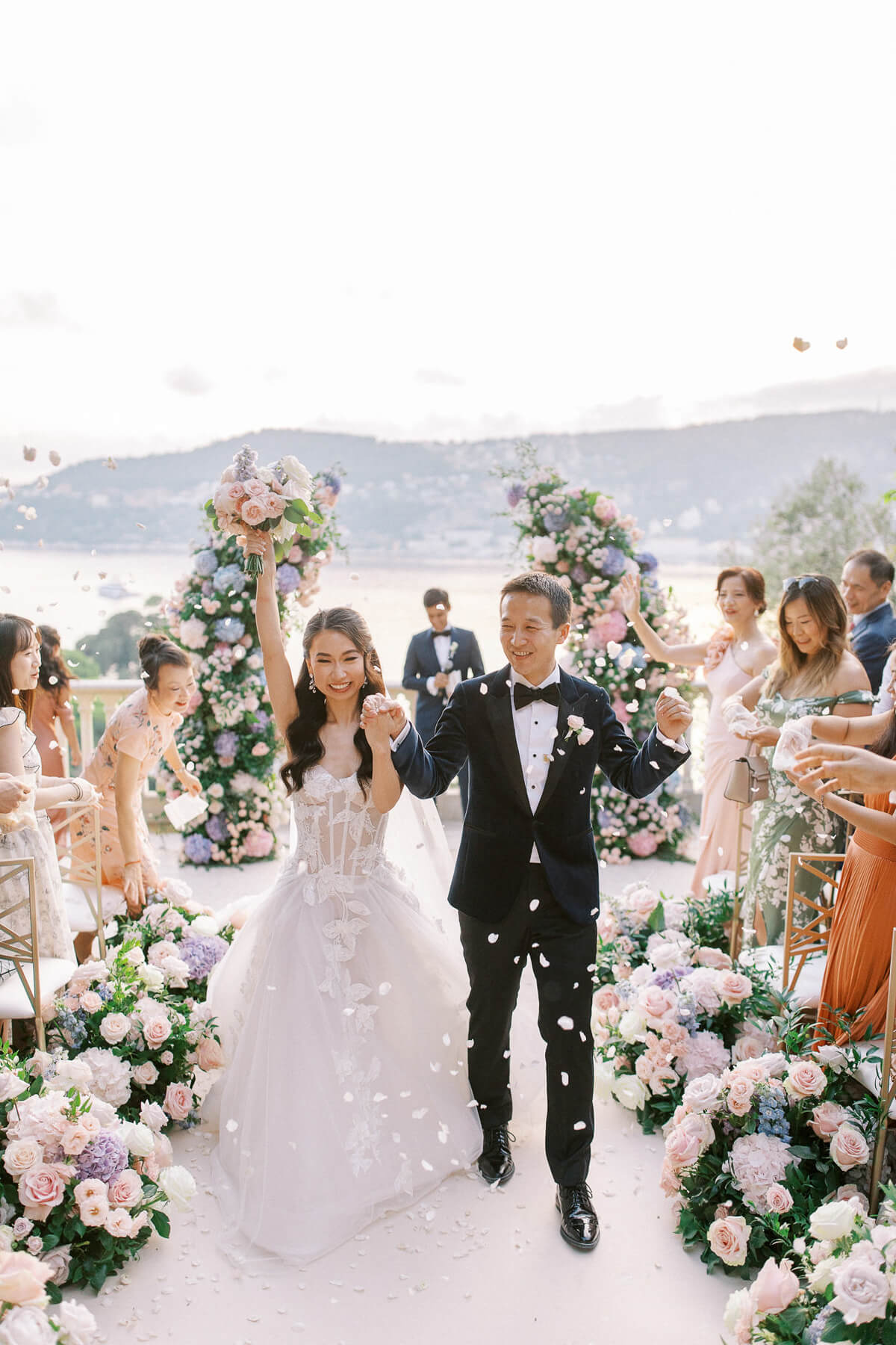 Bride and groom walking through flower petals during wedding exit at Villa Ephrussi de Rothschild with views of the French Riviera
